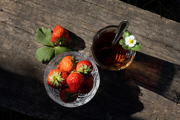 Cup of tea and wild strawberries on a wooden background