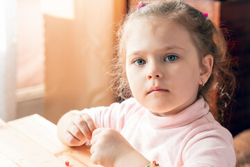 Fototapeta premium A little girl is engaged in needlework, making jewelry with her own hands, stringing multi-colored beads on a thread