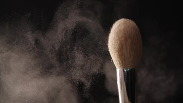Close-up of a makeup brush with face powder. Slow motion of white substance shaken off in black background. High quality FullHD footage
