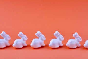 Row of ceramic rabbits on orange background.