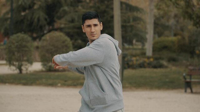 Hombre haciendo estiramientos, hombre con sudadera gris calentando antes del entrenamiento, hombre de pelo negro haciendo ejercicio en el parque, hombre girando los brazos y la cadera
