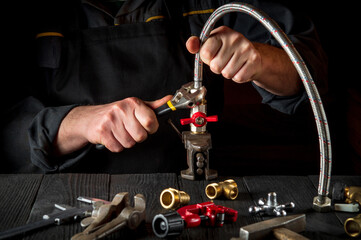 The plumber connects the brass fittings to the faucet with an adjustable wrench. Close-up of a foreman is hands while working in a workshop