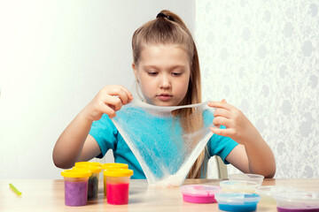 A blonde child is playing with a slime. Little beautiful caucasian girl is playing with many slimes. Play Slime Toy