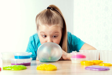 A blonde child blows a slime bubble. Play a slime toy. Making slime at home