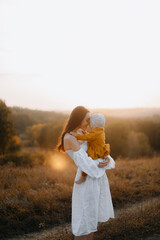 happy mother with baby in her arms. a young mother touches her forehead to the child. mother's love. young woman in a white dress with a baby in her arms