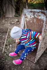 Adorable toddler girl sitting in wheelbarrow on farm. Farming and gardening for small children. Outdoor summer activities for little kids child plays with household appliances. Fun games in garden