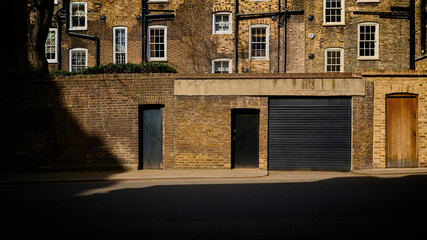 Rows of windows and doors at rear of old victorian terraced houses in london with black drainpipes and long shadows