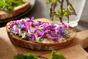 Obraz na płótnie Canvas Slice of bread with spring wild edible plants - young ground elder leaves, purple dead-nettle and lungwort flowers