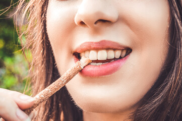 Beautiful girl cleans her  healthy white teeth with eco miswak stick. Smiling woman uses  organic toothbrush at nature. Traditional  islamic\arabian  teeth care with siwak.