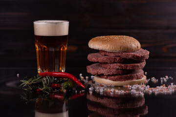 burger with raw cutlets on a dark background and a glass of beer. Low key. Carnivores, meat dishes. Selective focus