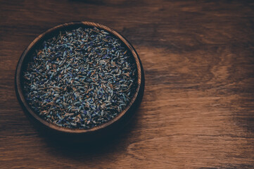 Dried lavender herb flowers in wooden bowl at light brown wooden background.