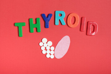 silhouette of the thyroid gland from pills and pink felt and the inscription thyroid on a red...
