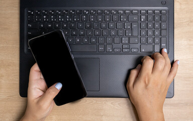 Black keyboard of a handheld computer with a cell phone and two hands of a white woman with a modern texture referring to work at home with technology, finance, credit among others.