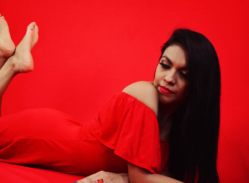 Chica latina acostada con las piernas levantadas con vestido rojo en estudio fotogr&aacute;fico