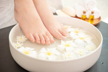 closeup view of woman soaking her feet in dish with water and flowers on wooden floor. Spa...