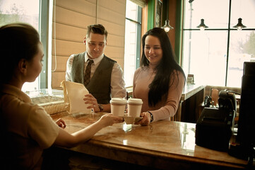 a barista serving a paper bag and a paper coffee cup to a customer in a coffee shop. making coffee in a cafe. 