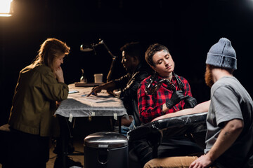 An experienced tattoo artist gives a tattoo to a white scandinavian hipster man with a red beard in his tattoo parlor.