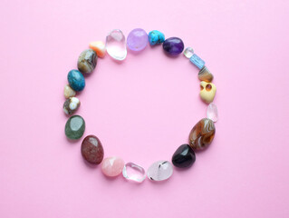 Semi-precious stones of different colors, raw and processed. Amethyst, rose quartz, agate, apatite, aventurine on a pink background.