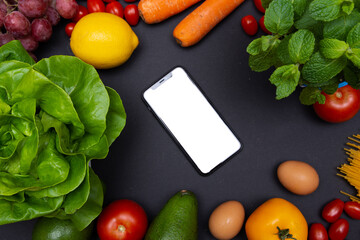 telefon z białym ekranem i miejscem na tekst, otoczony warzywami i owocami, zdrowa dieta i odżywianie - obrazy, fototapety, plakaty