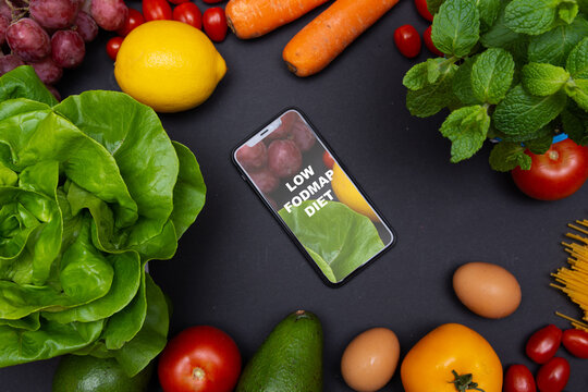 Telefon z tekstem low FODMAP diet na ekranie, otoczony warzywami i owocami, zdrowa dieta i odżywianie
