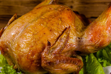 Plate with roasted whole chicken and lettuce leaves on a wooden table