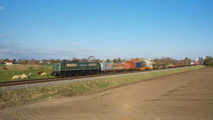 Fototapeta na wymiar Elektrische Güterzuglokomotive 151 124 fährt mit ihrem Containerzug an landwirtschaftlichen Anwesen zwischen München-Aubing und Puchheim vorbei