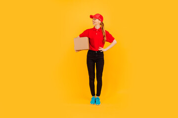 Smiling courier in red uniform holding cardboard box on isolated yellow background, fast and free delivery