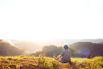 Young man sitting on the top of a mountain and watching the sunset in the mountains.