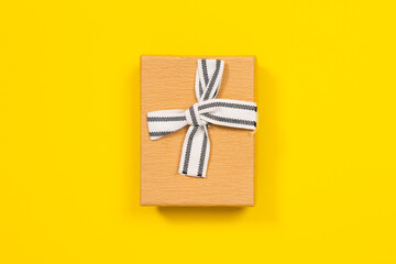 Close cardboard box with lid decorated with white ribbon bow for gift packaging on yellow background, top view, copy space for advertising text. Holiday stuff concept.