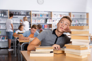 Fototapeta na wymiar Bored teenage boy trying to prepare for exam in school library