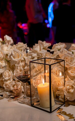 Vela en Cristalería Junto a Copa de Vino Frente a Flores Blancas Sobre Mesa de Boda y fondo de fiesta desenfado 