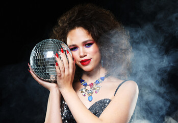 Naklejka premium Close up portrait of young african woman with bright make up holding disco balls over dark background