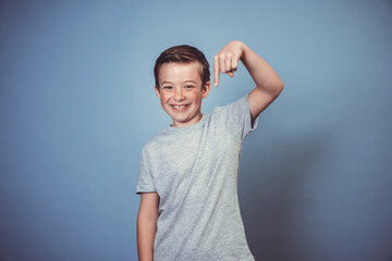 Obraz premium cool, young boy with grey t-shirt is posing in front of blue background in the studio