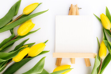 Yellow tulips flat lay on white background, empty picture frame, greeting card