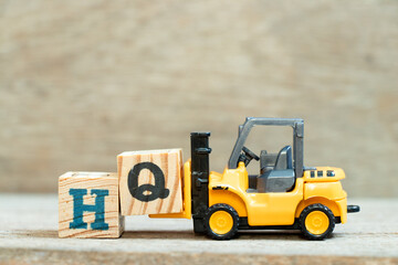 Toy forklift hold letter block q to complete word HQ (Abbreviation of headquarters) on wood background