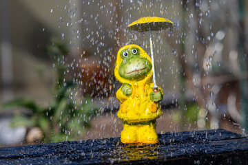 frog figure with yellow rain jacket standing in rain in spring and is protected by a rain umbrella, symbolizing unusual weather