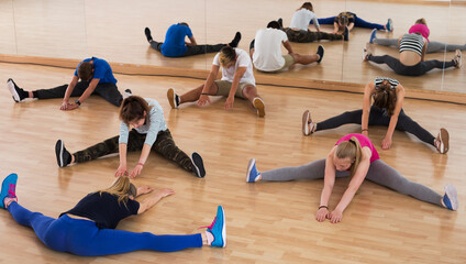 Group of teenage students with female mentor stretching in dance hall