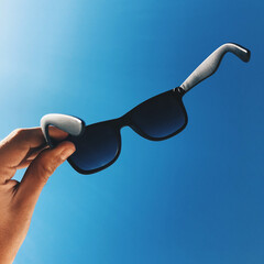 Hand holding sunglasses under the blue sky