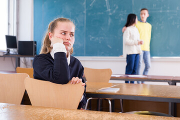 Portrait of unhappy girl sitting apart in class, having conflict with fellows students