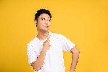 Fototapeta na wymiar Handsome healthy Asian young man smiling with pointing fingers isolated on a yellow background.