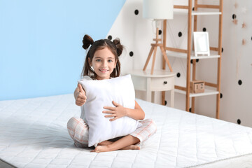 Morning of little girl showing thumb-up while sitting on bed with comfortable mattress