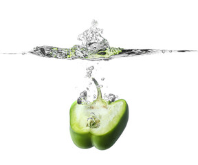 Falling of fresh cut bell pepper into water against white background