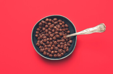 Bowl with chocolate corn balls on color background