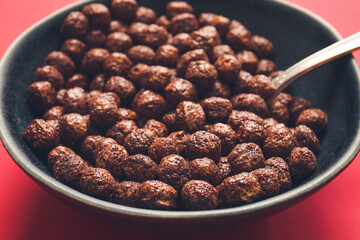 Bowl with chocolate corn balls on color background, closeup