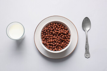 Bowl with chocolate corn balls and glass of milk on light background
