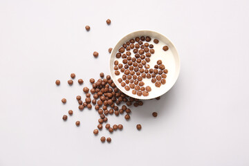 Bowl with chocolate corn balls and milk on light background