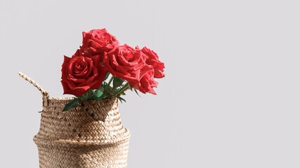 A bouquet of fresh red roses is in a wicker straw basket. Floral holiday layout. Copy space.