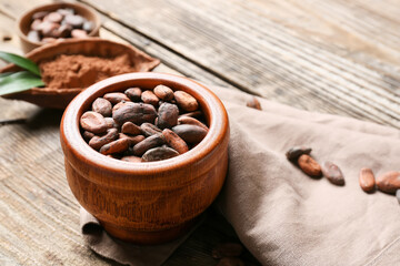 Bowl with cocoa beans on wooden background