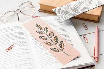 Books with bookmarks, glasses and stationery on light wooden background