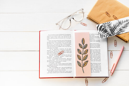 Books with bookmarks, glasses and stationery on light wooden background